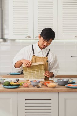 Asyalı Şef suşi sarmak için bambu hasırı hazırlıyor. Nori ve beyaz pirinçli klasik rulo. 