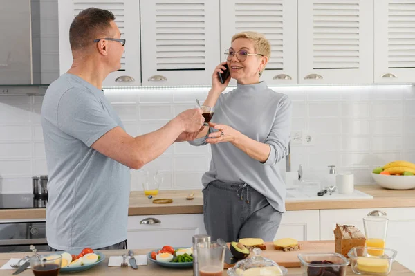 Ältere Paare beim gemeinsamen Kaffeefrühstück in der Küche. Frau telefoniert — Stockfoto