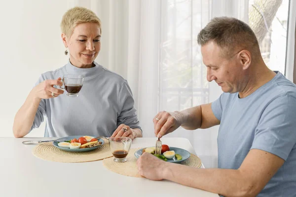 Gesunde reife Paare essen zusammen zu Mittag, sitzen auf dem Tisch, trinken Kaffee und lächeln — Stockfoto