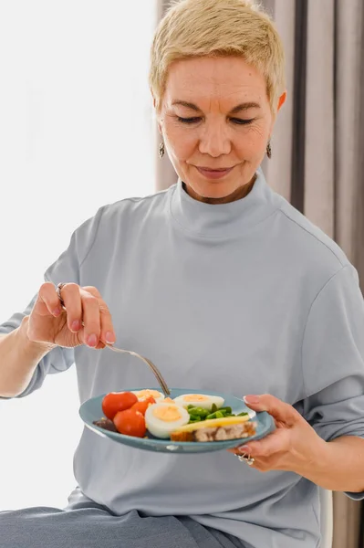 Dojrzałe kobiety jedzą śniadanie ze zdrowym jedzeniem na talerzu. Świeże warzywa i jajka. Koncepcja zdrowego żywienia — Zdjęcie stockowe