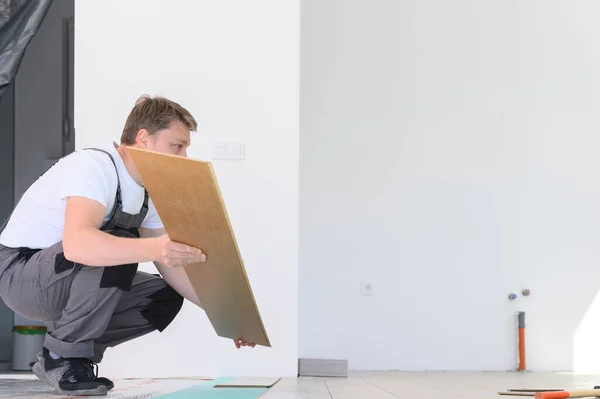 Processo de colocação de laminado na sala branca. Homem em uniforme instalar novo piso de madeira laminado, vista lateral — Fotografia de Stock