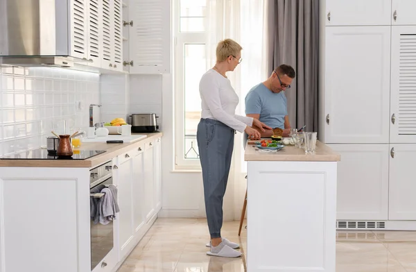 Porträt eines reiferen Paares, das zusammen kocht. Glückliche Seniorin kocht Frühstück für ihren Mann in weißer Küche — Stockfoto