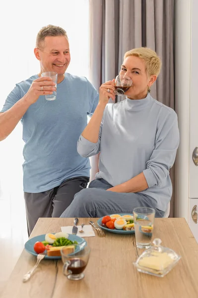 Gesunde reife Paare trinken Kaffee zum Frühstück in der Küche. Lächelnd, redend und lachend, Frau blickt in die Kamera — Stockfoto