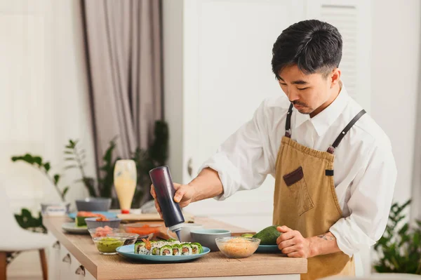 Asiatischer Koch macht Sushi-Rollen in der Küche. Fügt Sushi Sauce hinzu. Konzept der Essensausgabe — Stockfoto