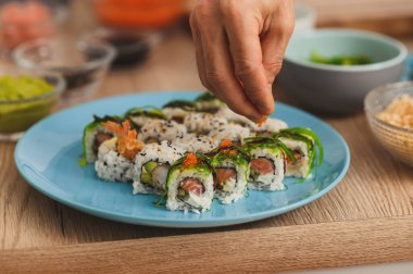 Sushi şefini kapat suşi yaparken pirincin üzerine kırmızı havyar serpiyor. Suşi yapma süreci, bir tabak ekmek.