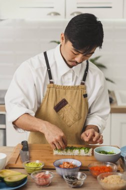 Asyalı şef suşi rulolarına malzeme ekler. İnternetten yemek servisi. Japon mutfağı: ekmek, soya sosu, wasabi. Sancak arkaplanı