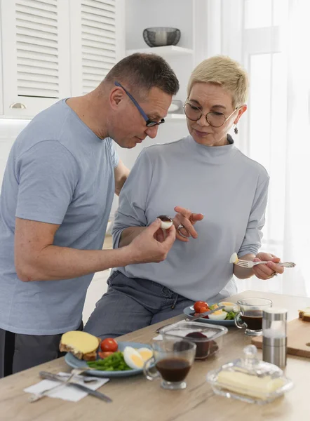 Ältere Männer und Frauen essen gesunde Lebensmittel mit frischem Gemüse in der Küche. Glückliches Rentnerleben, älteres Ehepaar — Stockfoto