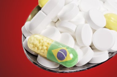 Spoon full of pills and a capsule with the flagdesign of Brazil.