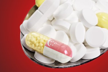 Spoon full of pills and a capsule with the flagdesign of Singapo
