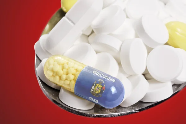 Spoon full of pills and a capsule with the flagdesign of Wiscons — Stockfoto