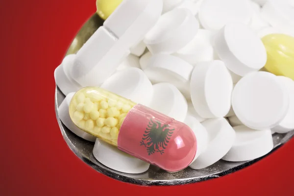 Spoon full of pills and a capsule with the flagdesign of Albania — Stockfoto