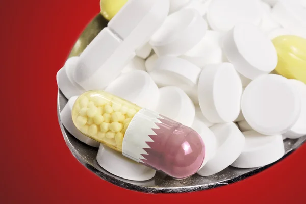 Löffel voller Pillen und eine Kapsel mit dem Flaggendesign von Katar.( — Stockfoto