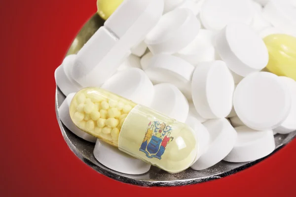 Colher cheia de pílulas e uma cápsula com o flagdesign de New Jer — Fotografia de Stock