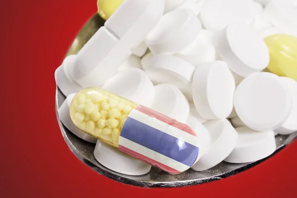 Spoon full of pills and a capsule with the flagdesign of Thailan — Stockfoto