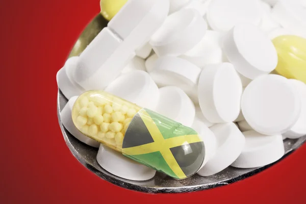 Spoon full of pills and a capsule with the flagdesign of Jamaica — стокове фото