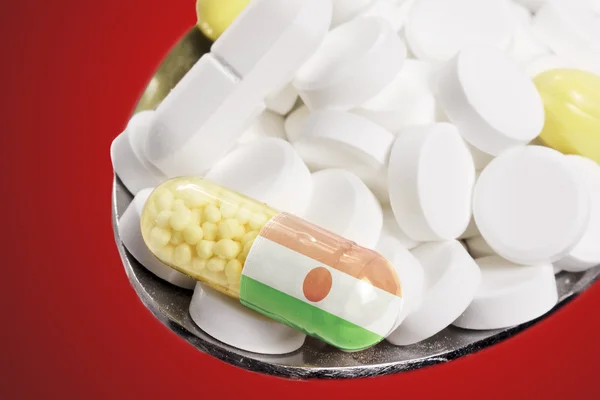 Spoon full of pills and a capsule with the flagdesign of Niger.( — Stockfoto