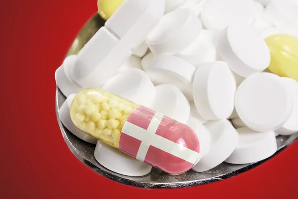 Spoon full of pills and a capsule with the flagdesign of Denmark — стокове фото