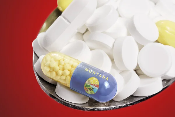 Spoon full of pills and a capsule with the flagdesign of Montana — Stockfoto