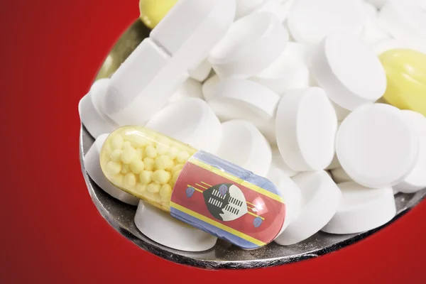 Spoon full of pills and a capsule with the flagdesign of Swazila — Stockfoto