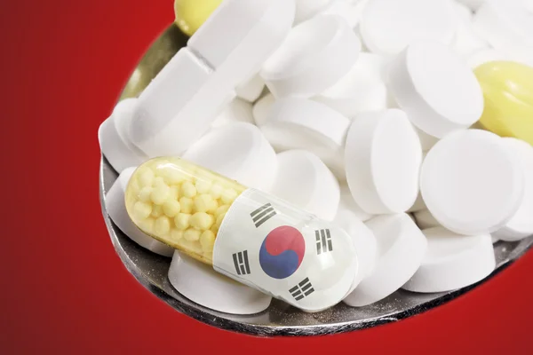 Spoon full of pills and a capsule with the flagdesign of South K 免版税图库照片