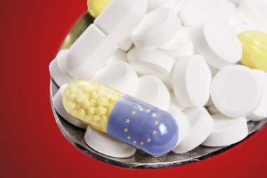 Spoon full of pills and a capsule with the flagdesign of Europe.