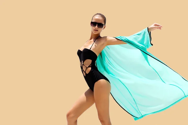Γυναίκα που χορεύει σε γυαλιά ηλίου μαύρο μαγιό και παραλία τυρκουάζ φόρεμα θέτει σε έγχρωμο φόντο. Εμφάνιση της μόδας. Μαλλιά επάνω. Κορίτσι μαύρισμα — Φωτογραφία Αρχείου