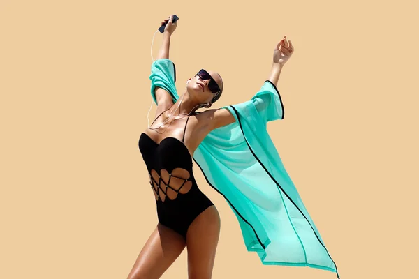 Donna danzante con cuffie in costume da bagno nero e occhiali da sole posa su sfondo a colori. Look alla moda. Su i capelli. Ragazza abbronzata — Foto Stock