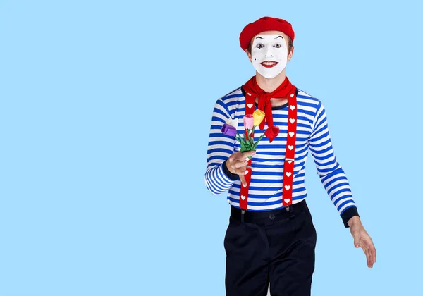 Pantomime mit Blumen. Emotional lustiger Schauspieler im Matrosenanzug, roter Baskenmütze posiert auf blauem Hintergrund. — Stockfoto