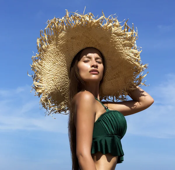 Woman in hat on beach. Beautiful gorgeous girl wearing green bikini poses near sea. Fashion look.Tropical photo — Stok fotoğraf