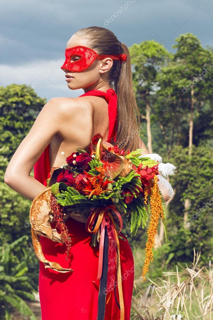 Beautiful woman in carnival mask with flowers wearing red dress poses on tropical sea view. Fashion masquerade look. Happy New Year festival. Phuket island, Thailand. Stock Photo by ©wehands 91579790