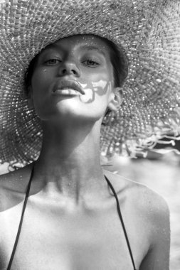 Woman in hat and black stylish swimsuit poses near swimming pool enjoying sun. Phuket island, Thailand. High fashion look.
