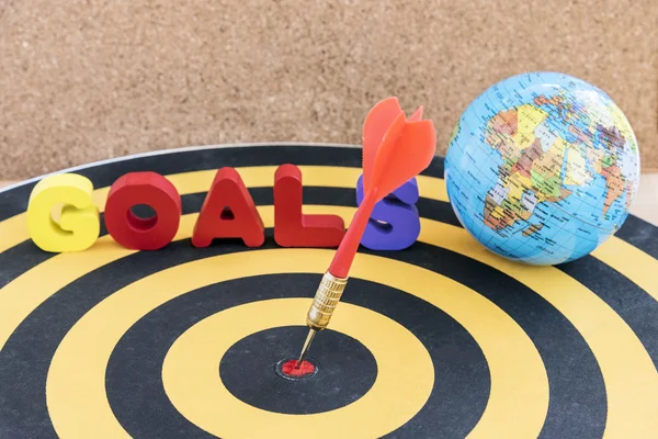 Dart target in bullseye on dartboard with goals and globe — Stock Photo, Image
