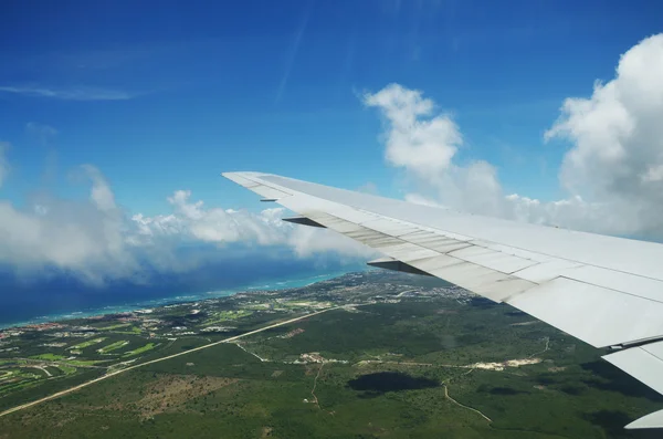 Ala de um avião voando acima das nuvens sobre a ilha tropical — Fotografia de Stock