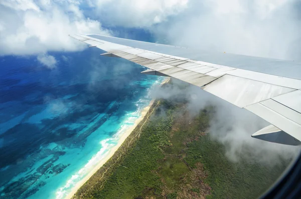 Ala de un avión volando por encima de las nubes sobre la isla tropical —  Fotos de Stock