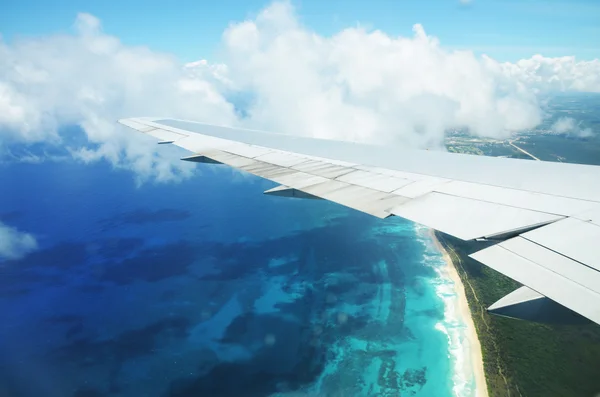 Ala de un avión volando por encima de las nubes sobre la isla tropical —  Fotos de Stock