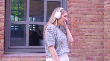 Neşeli beyaz kadın kulaklık takıyor dışarıda dans ediyor ve şarkı söylüyor mikrofon olarak akıllı telefonu kullanıyor, mutluluğu ifade ediyor, özgürlük, eğlence, müzik ve modern yaşam tarzı, yaratıcılık kavramı