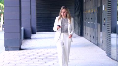 Modern ofisin dışında yürüyen profesyonel iş kadını akıllı telefon kullanıyor, mesajları ya da e-postaları kontrol ediyor, iletişim konsepti, teknoloji, hareketlilik, başarı, liderlik ve yoğun kurumsal yaşam tarzı
