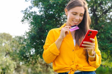 Akıllı telefon kullanan ve dışarıda elinde fotokopi alanı olan gülümseyen genç bir kadın. Çevrimiçi alışveriş, dijital ödeme, modern yaşam tarzı, e ticaret, finans, bağlantı, teknoloji, özgürlük