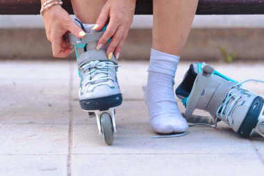 Açık havada bir bankta otururken paten bağlayan, beyaz çorap giyen ve paten seansına hazırlanan, boş zamanları, sporu, fitness 'i, özgürlüğü, enerjiyi temsil eden birinin yakın plan fotoğrafını çekin.