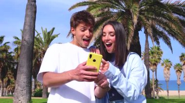 Palmiye ağaçlarıyla dolu yeşil parktaki genç çift sarı akıllı telefonu bir arada tutarken gördükleri eğlenceli yaz anının keyfini çıkarırken şaşırdılar ve heyecanlandılar.