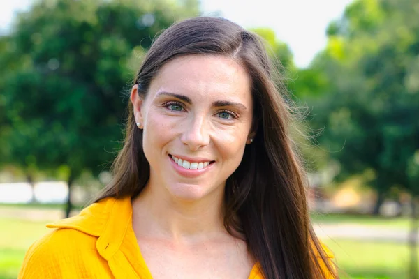 Sarı gömlekli mutlu beyaz kadın portresi. Güneşli parkta gülümseyen ve kameraya bakan. Doğal güzellik, kendine güven ve yaşam tarzı ve insanların kavramları için pozitif ifade..