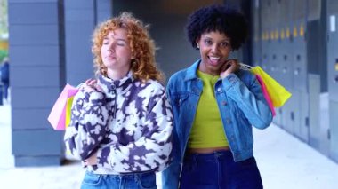 Alışveriş yaptıktan sonra dışarı çıkan iki neşeli genç kadın, neşe içinde gülümseyen ve konuşan, renkli çantalar taşıyan, arkadaşlık konsepti, yaşam tarzı, eğlence, moda, mutluluk ve kentsel modern hayat.