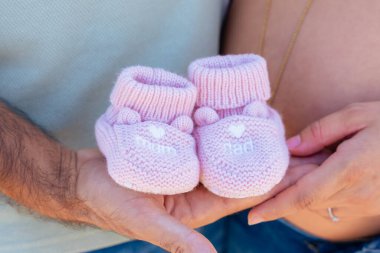 Hamile çiftin ellerinde pembe bebek paçası, annelik kavramı, aile sevgisi, beklenti, hamilelik süresince yeni bir hayat ve mutluluk, gelecekteki bebek kızının gelişinin sembolü..