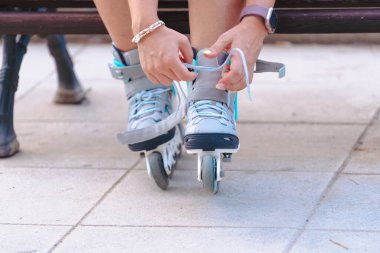 Açık havada bir bankta otururken paten bağlayan, beyaz çorap giyen ve paten seansına hazırlanan, boş zamanları, sporu, fitness 'i, özgürlüğü, enerjiyi temsil eden birinin yakın plan fotoğrafını çekin.