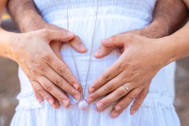 Hamile çift elleriyle göbeğine kalp şekli veriyor, sevgi, annelik, ebeveynlik, müstakbel bebek, aile bağı, şefkat, beklenti, bağlantı, mutluluk, şefkat ve beklenti kavramı..