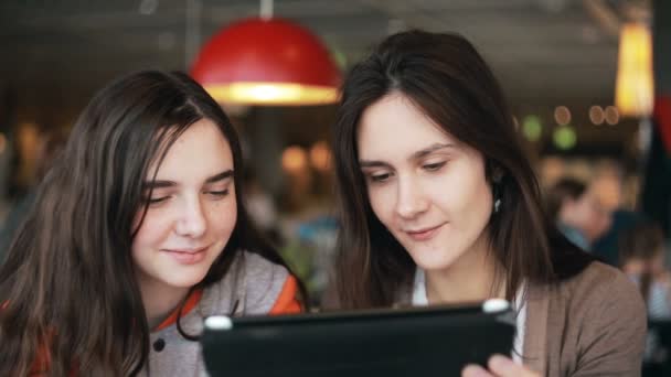 Dos hermanas chicas usando la tableta hablando en la cafetería — Vídeos de Stock