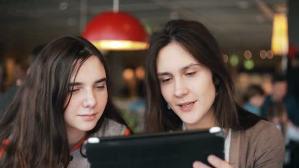 Duas meninas irmãs usando tablet falando no café — Vídeo de Stock