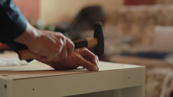 Hombre ensambla partes de muebles usando un martillo . — Vídeos de Stock