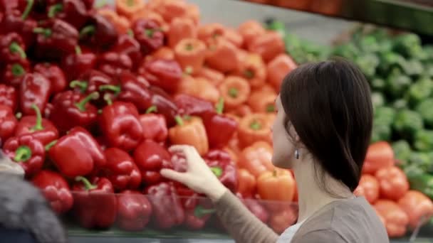 Jonge vrouw kiest paprika op opslagplanken. — Stockvideo