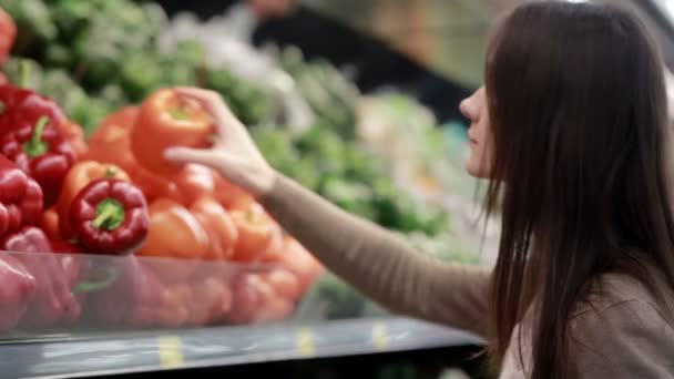 Jonge vrouw kiest paprika op opslagplanken. — Stockvideo